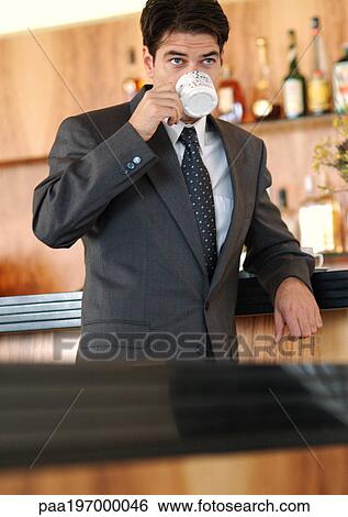 Businessman standing at bar, drinking out of coffee cup. View Large Photo Image Stock Photograph - Businessman standing at bar, drinking out of coffee cup.. Fotosearch