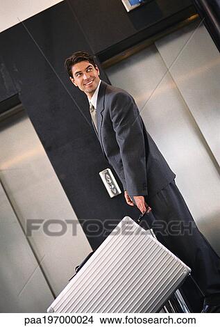 Businessman standing near elevators with suitcase, looking over shoulder View Large Photo Image Picture - Businessman standing near elevators with suitcase, looking over shoulder. Fotosearch