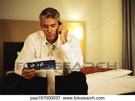 Businessman talking on cell phone, looking at ticket View Large Photo Image Stock Photo - Businessman talking on cell phone, looking at ticket. Fotosearch