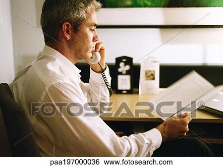 Businessman talking on phone, looking at paper, side view, close-up View Large Photo Image Stock Photograph - Businessman talking on phone, looking at paper, side view, close-up. Fotosearch