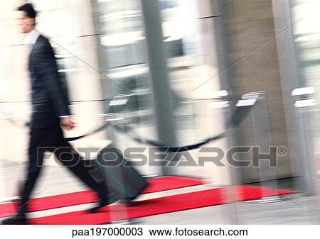 Stock Image - Businessman walking with luggage, side view, blurred.. Fotosearch