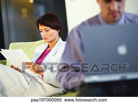 Stock Photography - Businesswoman looking at document near businessman on computer, blurred.. Fotosearch