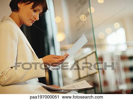 Stock Image - Businesswoman looking at documents near window.. Fotosearch