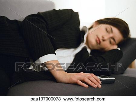Stock Photo - Businesswoman lying on couch, eyes closed, hand on cell phone. Fotosearch