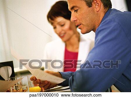 Stock Image - Businesswoman sitting next to businessman reading document, side view, close-up.. Fotosearch