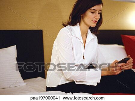 Businesswoman sitting on bed, using cell phone. View Large Photo Image Stock Image - Businesswoman sitting on bed, using cell phone.. Fotosearch