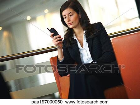 Stock Image - Businesswoman sitting, using cell phone.. Fotosearch