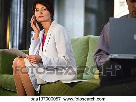 Stock Photo - Businesswoman sitting using cell phone, man using laptop. Fotosearch
