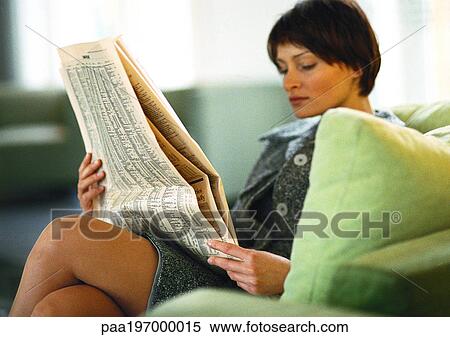 Stock Photography - Businesswoman sitting with legs crossed, reading paper.. Fotosearch