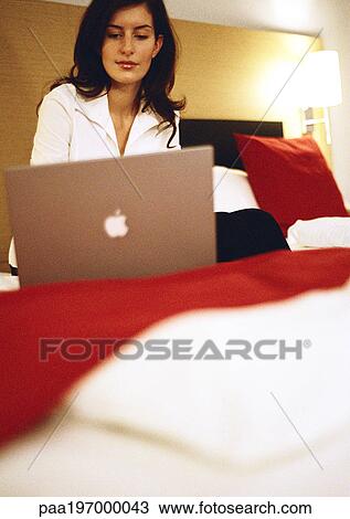 Stock Image - Businesswoman working on laptop computer on bed.. Fotosearch