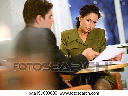 Stock Image - Man and woman sitting, looking at document. Fotosearch