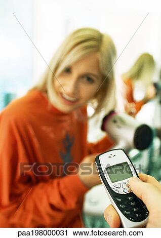 Man's hand holding cell phone, woman blow-drying hair View Large Photo Image Stock Image - Man's hand holding cell phone, woman blow-drying hair. Fotosearch