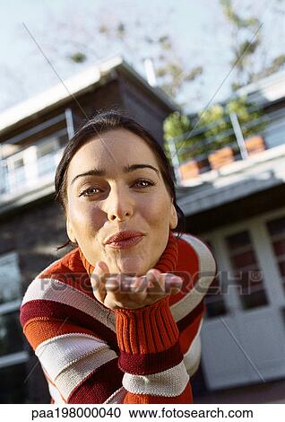 Woman leaning forward blowing a kiss, head and shoulders, close-up, house in background, low angle view View Large Photo Image Stock Image - Woman leaning forward blowing a kiss, head and shoulders, close-up, house in background, low angle view. Fotosearch