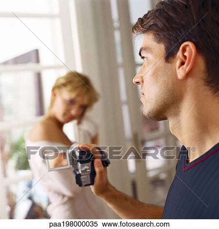 Young man holding camcorder, filming young woman in background View Large Photo Image Stock Photography - Young man holding camcorder, filming young woman in background. Fotosearch