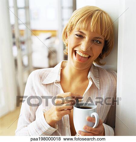 Young woman leaning against wall and holding a mug, sticking her tongue out. View Large Photo Image Stock Photo - Young woman leaning against wall and holding a mug, sticking her tongue out.. Fotosearch