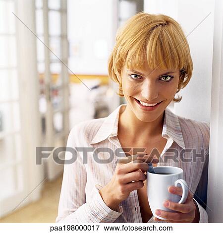 Young woman leaning against wall, holding mug, smiling. View Large Photo Image Stock Photo - Young woman leaning against wall, holding mug, smiling.. Fotosearch