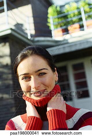 Young woman standing in front of a house with hands on neck, smiling at camera View Large Photo Image Stock Image - Young woman standing in front of a house with hands on neck, smiling at camera. Fotosearch