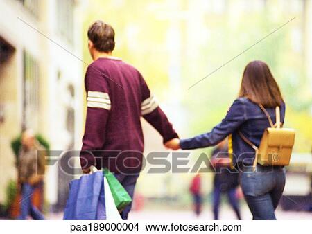 Picture - Couple shopping together, holding hands, view from behind.. Fotosearch