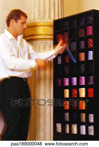 Stock Photo - Man holding neck tie, looking at it.. Fotosearch