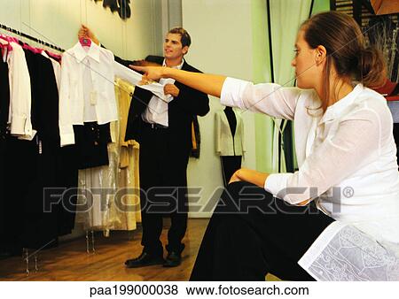 Man holding up woman's blouse, woman sitting and pointing, in clothing store View Large Photo Image Stock Photo - Man holding up woman's blouse, woman sitting and pointing, in clothing store. Fotosearch