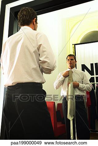 Man looking into mirror, holding necktie up to neck. View Large Photo Image Stock Photo - Man looking into mirror, holding necktie up to neck.. Fotosearch