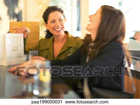 Two woman sitting at bar laughing, shopping bags to the side. View Large Photo Image Stock Image - Two woman sitting at bar laughing, shopping bags to the side.. Fotosearch