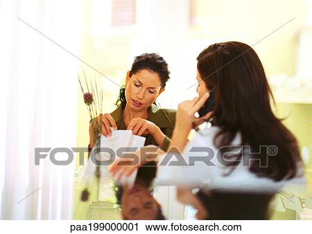 Two women sitting together, one on cellular phone, one looking in shopping bag. View Large Photo Image Stock Image - Two women sitting together, one on cellular phone, one looking in shopping bag.. Fotosearch