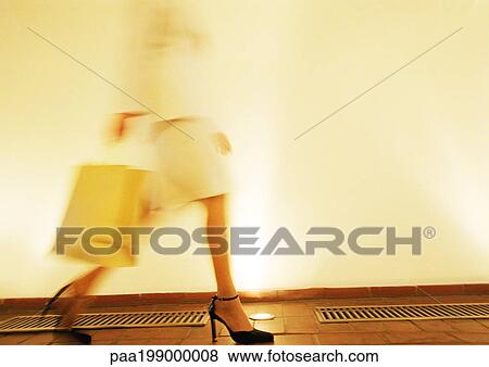 Stock Photo - Woman in heels walking with shopping bag, side view, blurred motion. Fotosearch