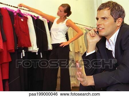 Woman looking at clothes in store behind man on cellular phone. View Large Photo Image Stock Photograph - Woman looking at clothes in store behind man on cellular phone.. Fotosearch