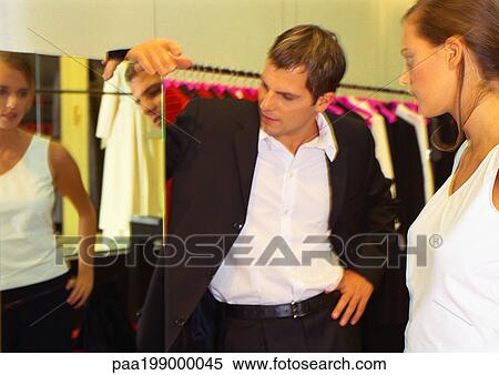 Stock Photography - Woman looking into mirror inside clothing store, man looking at woman in mirror.. Fotosearch