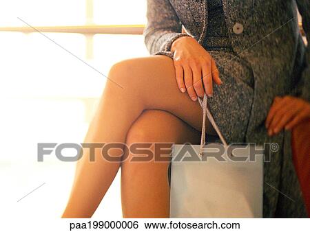 Woman sitting, legs crossed, holding shopping bag, mid-section View Large Photo Image Stock Photograph - Woman sitting, legs crossed, holding shopping bag, mid-section. Fotosearch