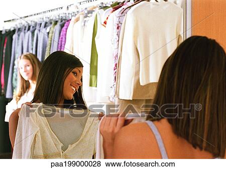 Young woman holding shirt up, looking into mirror in clothing shop View Large Photo Image Stock Photo - Young woman holding shirt up, looking into mirror in clothing shop. Fotosearch