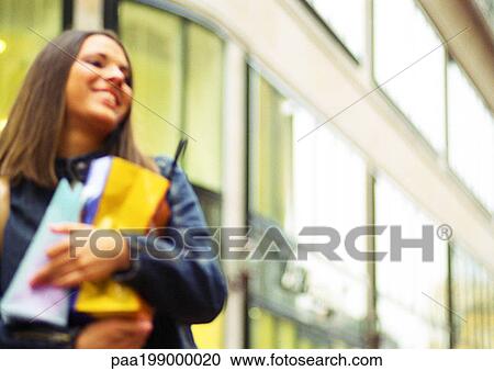 Stock Image - Young woman holding shopping bags in arms, smiling, blurred.. Fotosearch
