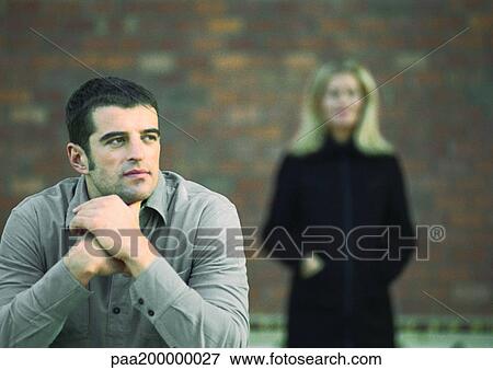 Man sitting, woman blurred in background. View Large Photo Image Stock Photo - Man sitting, woman blurred in background.. Fotosearch