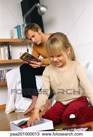 Daughter looking at objects in box, father reading nearby. View Large Photo Image Stock Image - Daughter looking at objects in box, father reading nearby.. Fotosearch