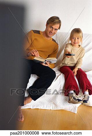 Stock Photo - Father sitting next to daughter with remote control.. Fotosearch