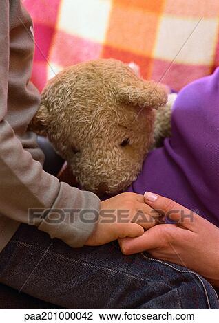 Stock Image - Woman and child holding hands, teddy bear between them. Fotosearch