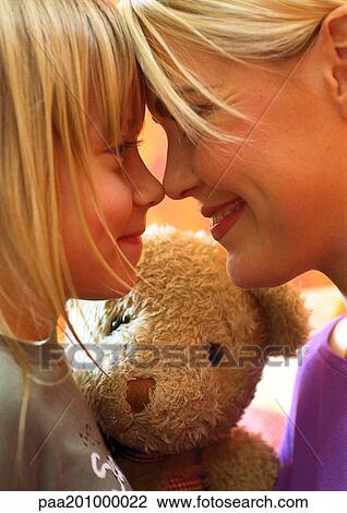 Stock Image - Woman and little girl, nose to nose, teddy bear in background. Fotosearch