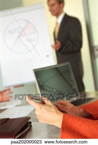 Stock Image - Businessman and businesswoman, businessman in background giving presentation, blurred.. Fotosearch