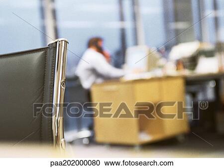 Stock Image - Businessman sitting at desk talking on phone, blurred.. Fotosearch