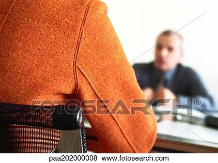 Stock Photo - Businessman sitting at table blurred in background, person's back in foreground.. Fotosearch