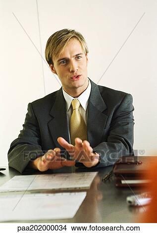 Picture - Businessman sitting at table talking.. Fotosearch