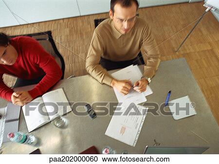 Stock Image - Businessmen sitting at table in meeting room.. Fotosearch