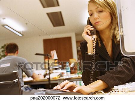Stock Image - Businesswoman dialing phone in office.. Fotosearch
