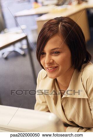 Stock Image - Businesswoman smiling, working on computer.. Fotosearch