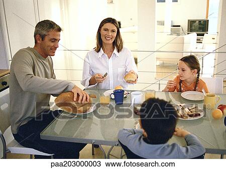 Stock Image - A family of four sitting down and eating.. Fotosearch