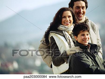 Adult man and woman with boy, woman's hand on boy's shoulder, waist up, mountain landscape blurred in background View Large Photo Image Picture - Adult man and woman with boy, woman's hand on boy's shoulder, waist up, mountain landscape blurred in background. Fotosearch