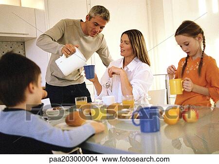 Picture - Family eating breakfast together, father pouring drinks.. Fotosearch