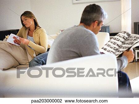 Stock Image - Man and woman sitting on couch reading.. Fotosearch