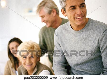 Stock Photo - Man looking away, waist up, partial view, three adults smiling in background. Fotosearch